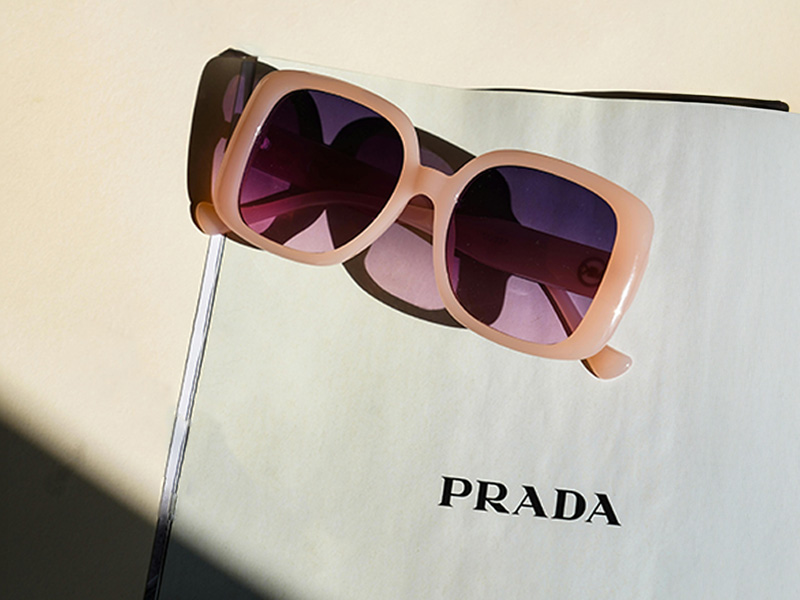 Rosa übergroße Prada-Sonnenbrille mit violetten Gläsern auf einer Zeitschriftenseite mit Prada-Logo