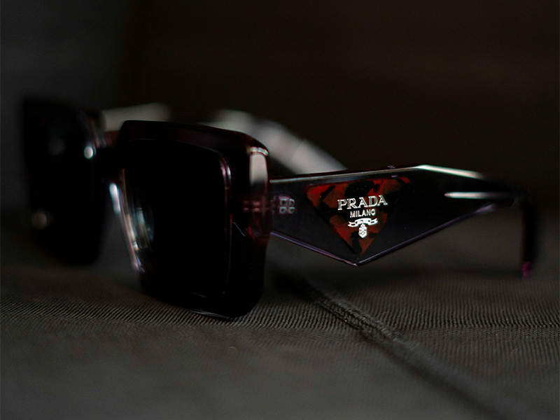 Nahaufnahme eines Prada Milano-Logos auf dem Bügel einer dunklen Sonnenbrille, das die Markendetails hervorhebt, die zur Authentifizierung echter Prada-Sonnenbrillen verwendet werden