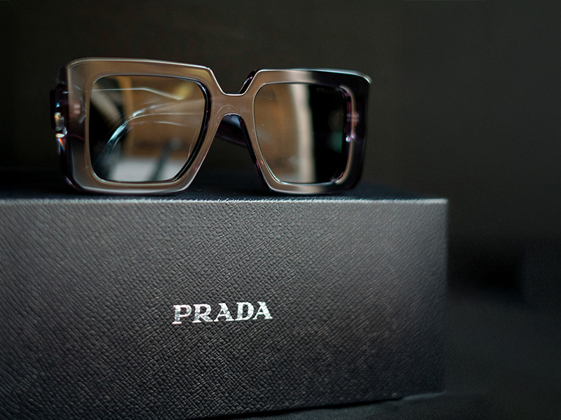 Authentische Prada-Sonnenbrillen werden auf einem strukturierten schwarzen Prada-Etui präsentiert, wobei die Premium-Verpackung als Echtheitshinweis dient